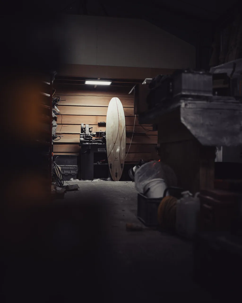 A finished board stands at the far end of the dark workshop.
