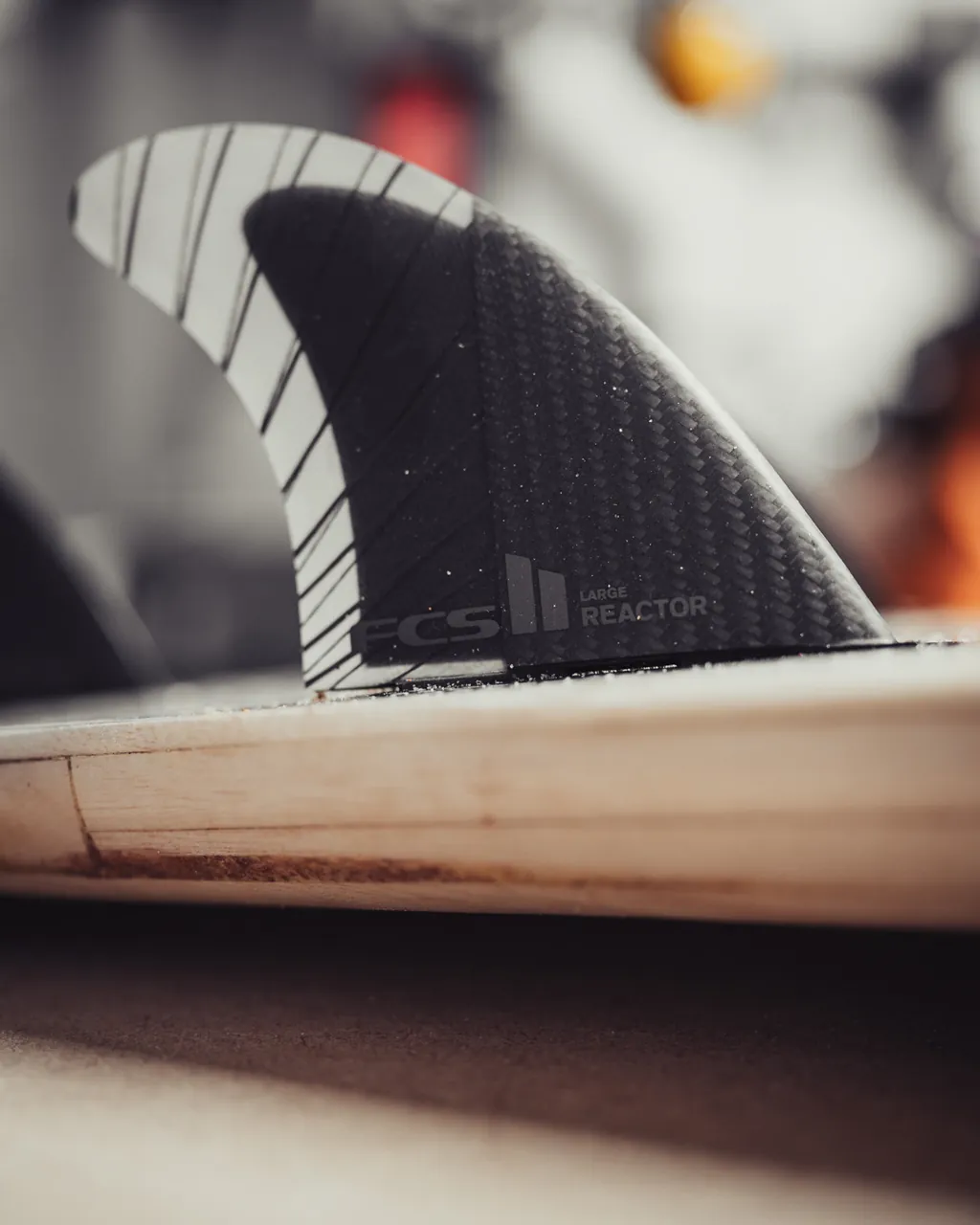 A black FCS fin set into the pale timber of the board.