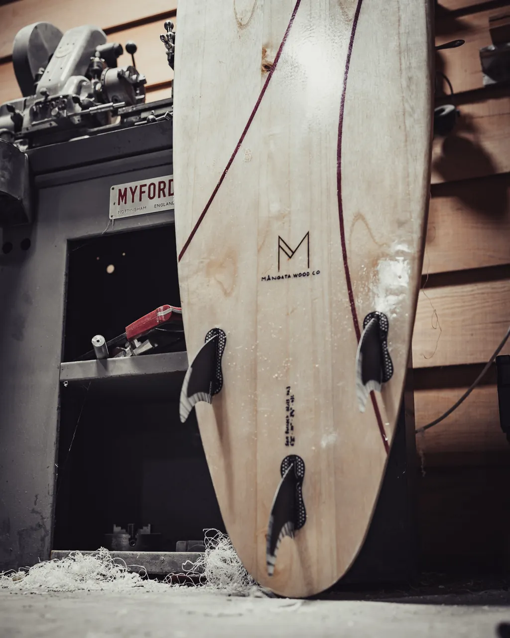 The tail of a board and its fins, beside an old lathe.