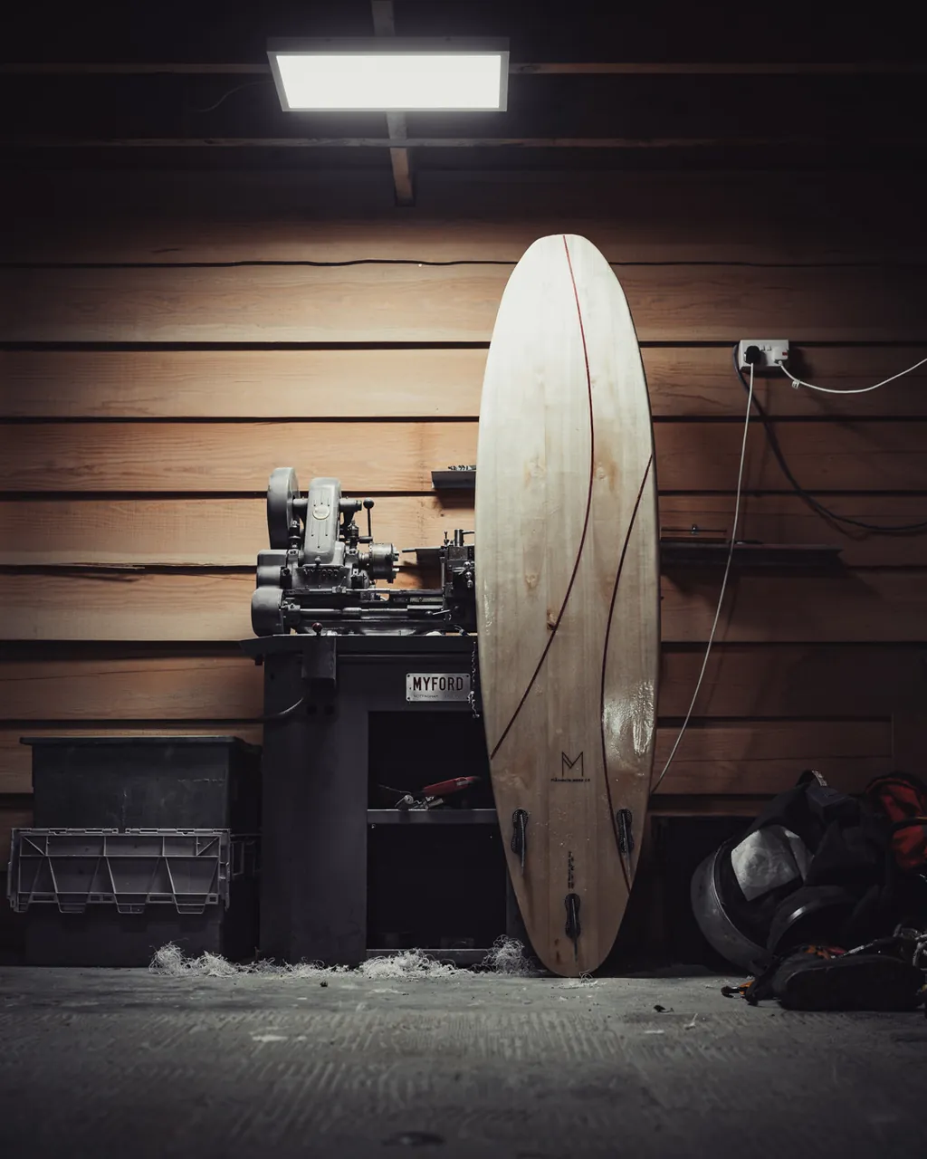 A finished board stands against the timber-clad workshop wall, lit from above.