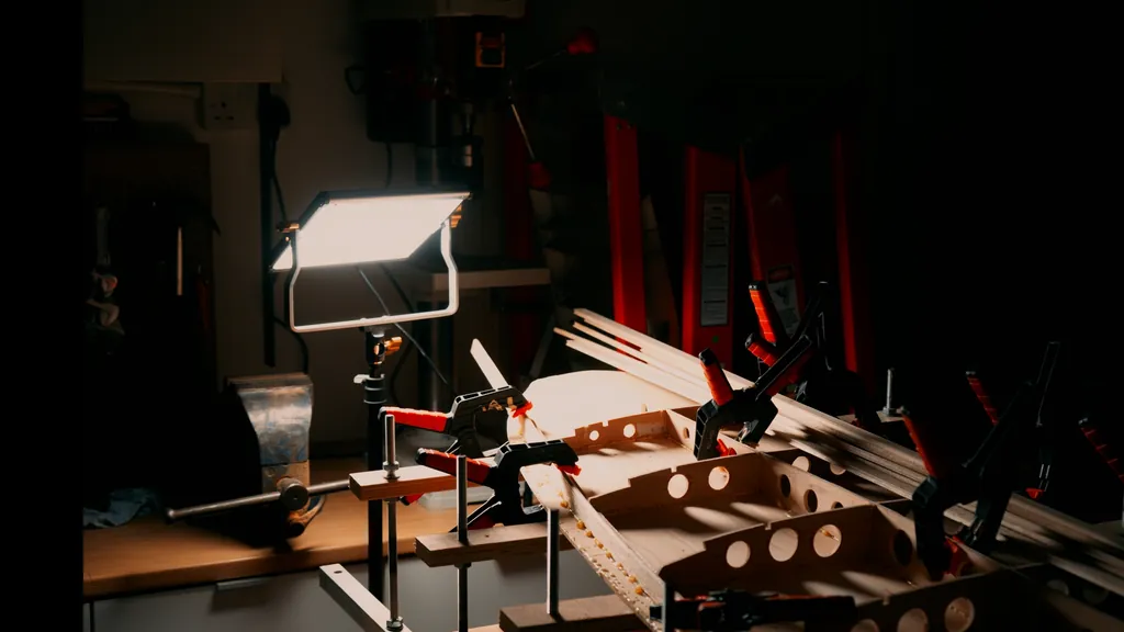 A board skeleton clamped on the bench under a work light: a spine with ribs set across it, each rib cut through with round holes.